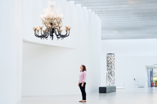 Woman looks up at a large glass chandelier in a white gallery